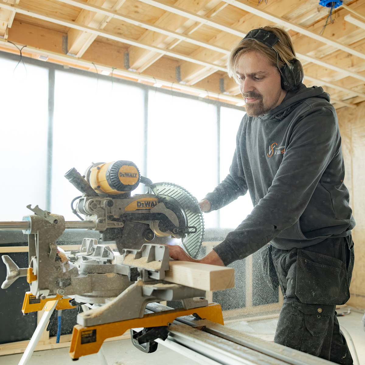Timmerman van Vida Stone zaagt hout met een afkortzaag